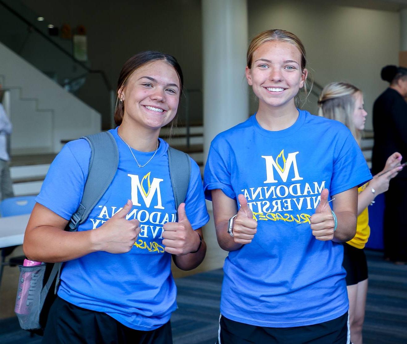 2 students smiling with their thumbs up in the Franciscan Center for 2023 Orientation